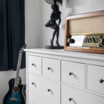 Chic interior with black lamp, acoustic guitar, and vintage radio on a white dresser.